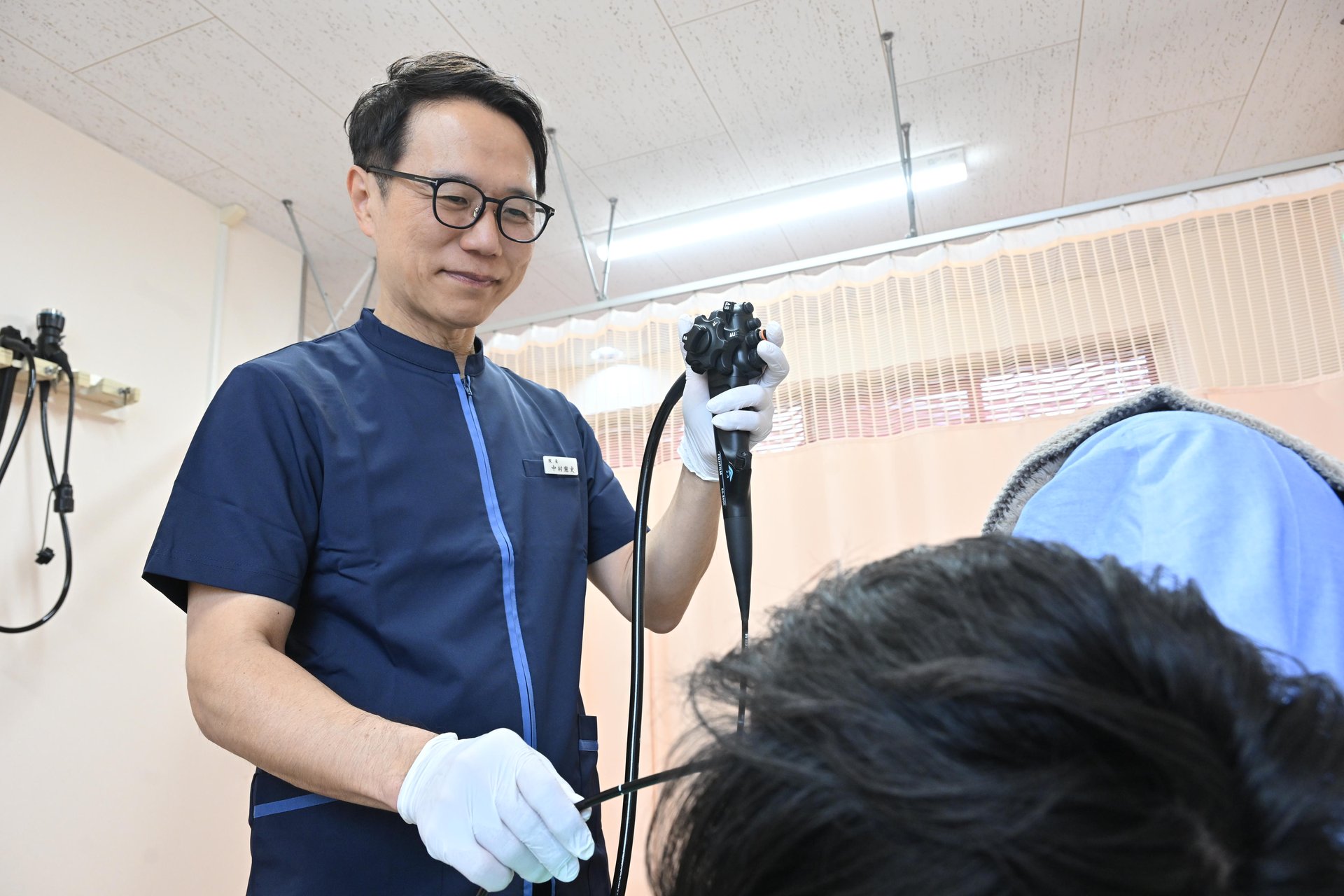 内視鏡室／胃カメラ・大腸カメラ - 院長 内視鏡を持って正面立ちポーズ（1枚もの）。