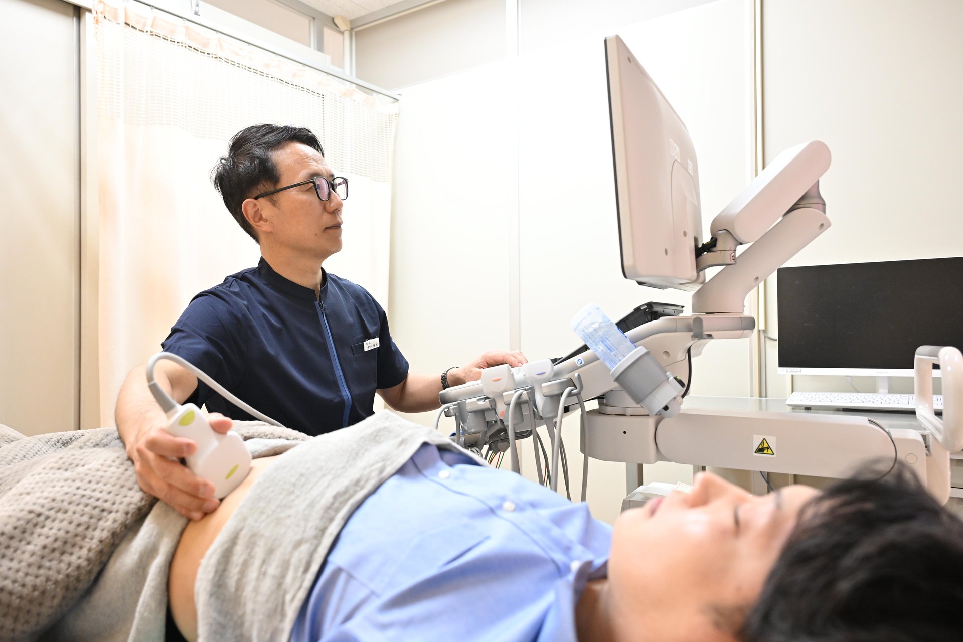 院長がエコー機器で患者の腹部を検査している様子
