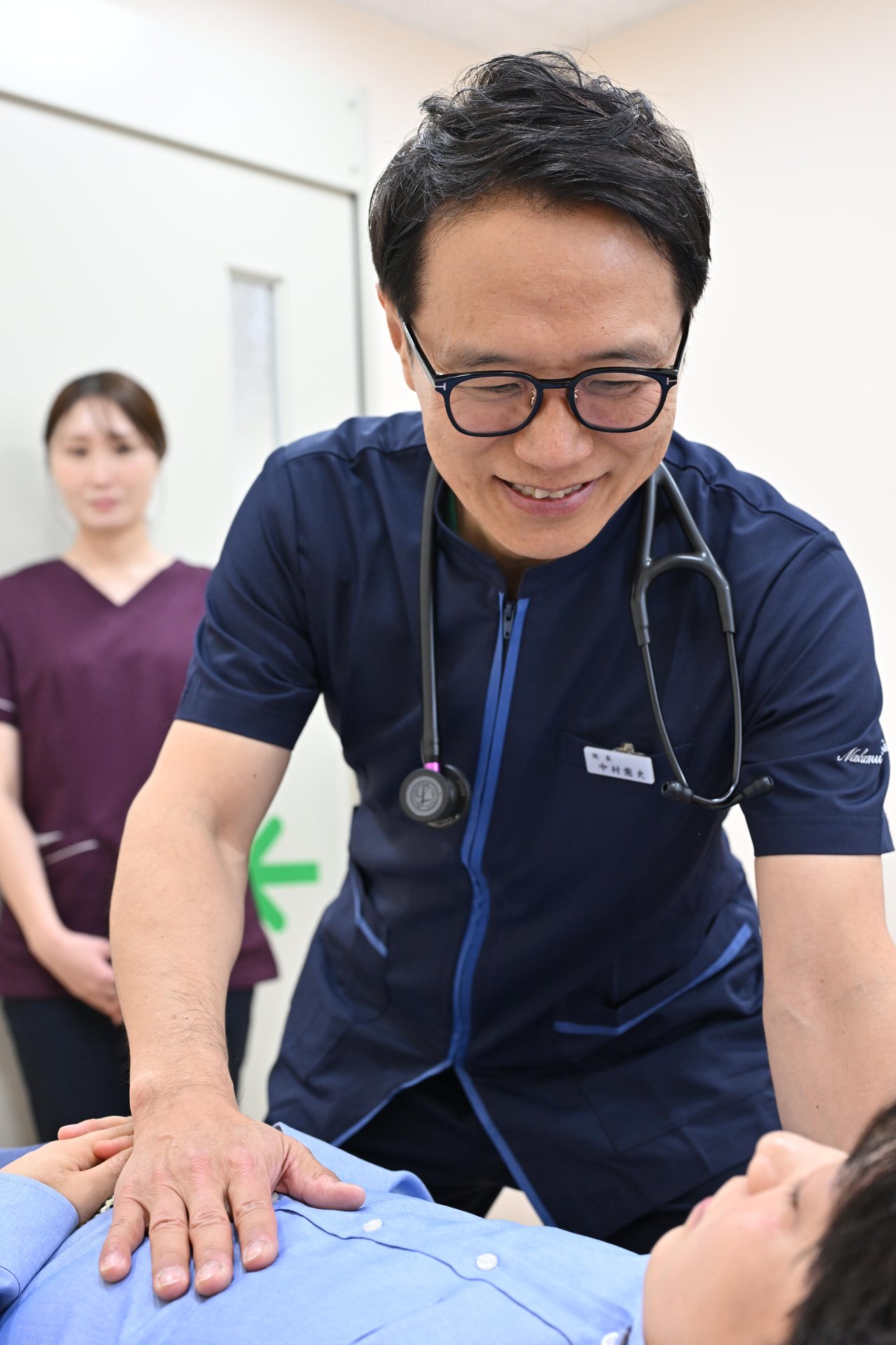 院長が立位で患者の腹部を触診する様子